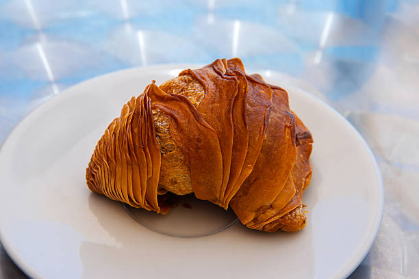 A traditional sfogliatella pastry on a white ceramic plate atop a shiny metallic table in outdoor cafe in Italy