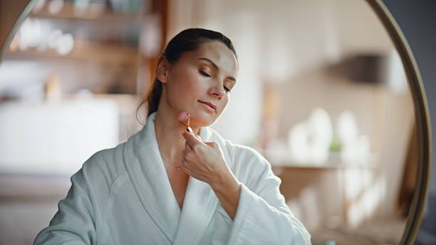 istock Woman using face roller for self massaging beautiful face in mirror closeup. 2225279157