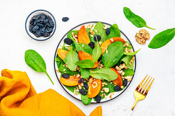 istock Autumn vegan persimmon salad with walnuts, blue raisin and spinach, white background, top view 2225281038