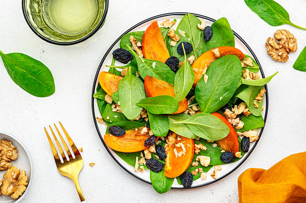 istock Autumn vegan salad with fresh persimmon, walnuts, raisin and spinach, white background, top view 2225281043