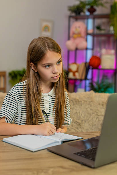istock Child girl kid doing online homework on laptop and writing math notes sitting at home table 2225282723
