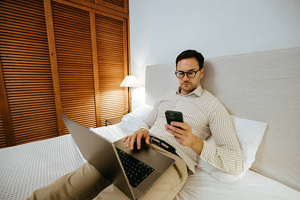 istock Young well dressed businessman using smart phone while working on laptop at hotel room 2225282887