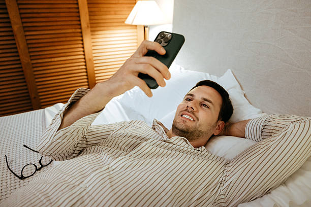 istock Cheerful young businessman using smart phone while relaxing on a bed 2225282905