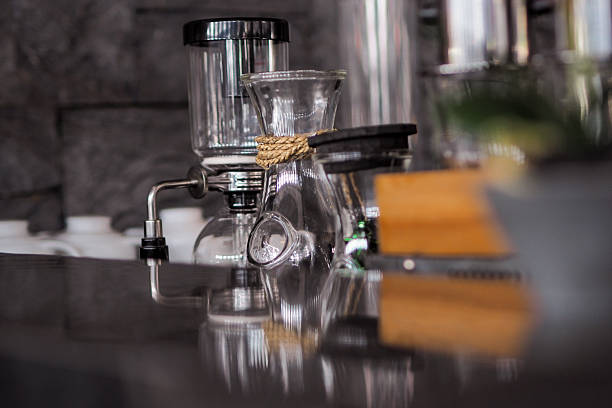 istock close-up, slightly blurred shot of a siphon coffee maker, also known as a vacuum coffee maker, on a reflective surface. The coffee maker is made of clear glass with a visible thermometer 2225284314