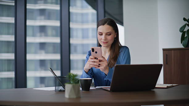 istock Smiling entrepreneur reading sms cellphone at laptop workplace. Elegant brunette 2225284583