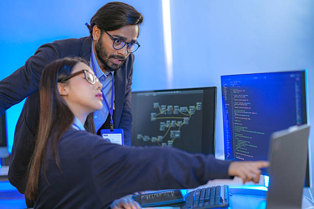 istock Asian female AI programmer and Indian male data analyst reviewing code on a monitor. Diverse tech professionals collaborating on an artificial intelligence project in a modern office. 2225285708
