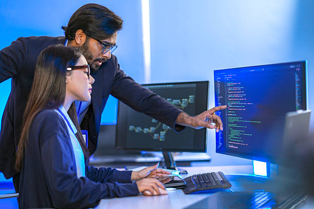 istock Asian female AI programmer and Indian male data analyst reviewing code on a monitor. Diverse tech professionals collaborating on an artificial intelligence project in a modern office. 2225285768