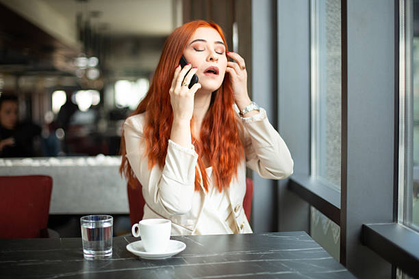 Redhead businesswoman looking stressed while having a phone call in a cafe