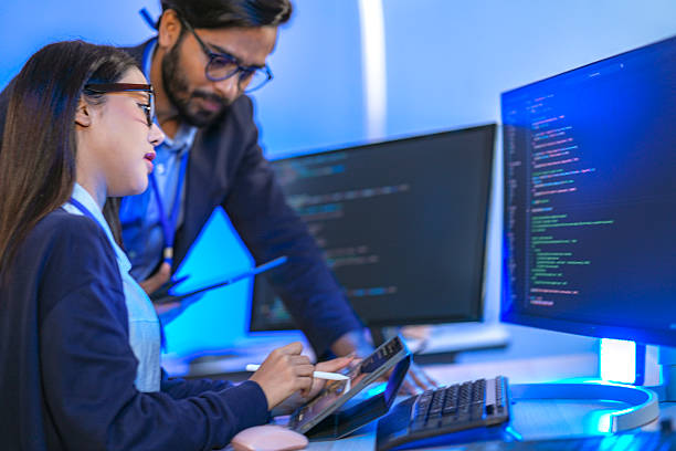 istock Asian female AI programmer and Indian male data analyst reviewing code on a monitor. Diverse tech professionals collaborating on an artificial intelligence project in a modern office. 2225286632