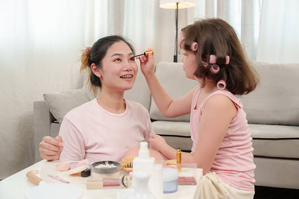 istock Asian young daughter applying makeup with serious expression on mother's face during beauty session, warm nurturing moment, emotional bonding, trust and encouragement growing at cozy family home. 2225297259