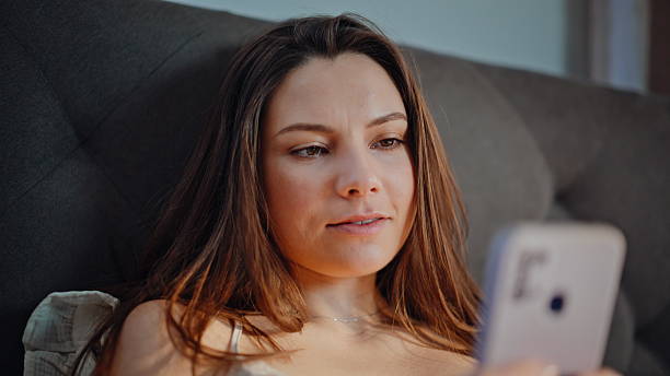 istock Smiling woman reading cellphone message lying modern bedroom interior closeup. 2225297853