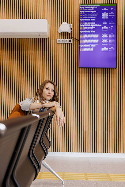istock Young woman sitting alone at a modern bus terminal, resting on a bench while waiting for departure, looking thoughtful and calm under schedule board. Bus station 2225309427