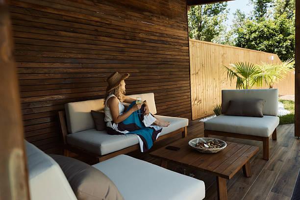 istock Smiling woman with a hat relaxing on sofa at patio. 2225309609