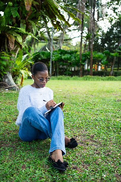 istock Young woman writing in notebook sitting on grass in park 2225311988