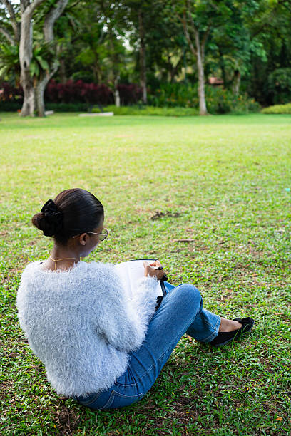 istock Young woman writing in notebook while sitting on grass in park 2225311990
