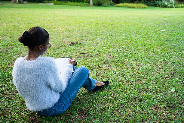 Young woman writing in notebook while sitting on grass in park