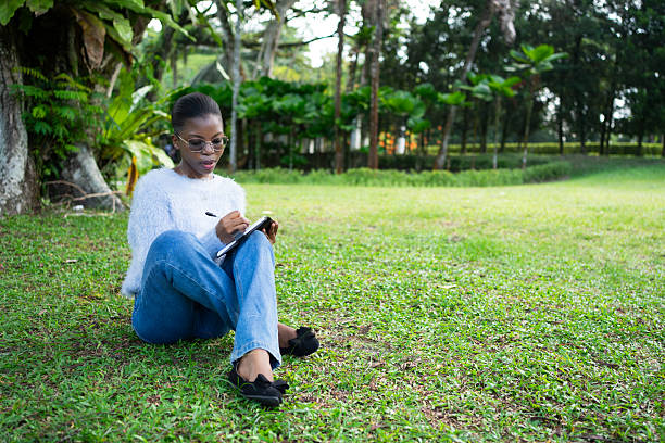 istock Young woman writing in notebook while sitting on grass in park 2225312004