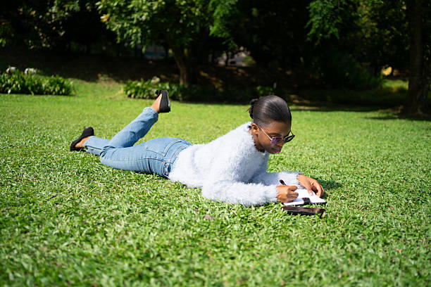 istock Young woman lying on grass writing in notebook in a park 2225312040