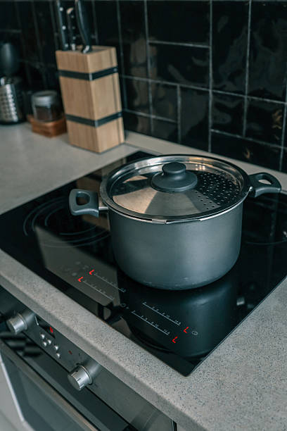 istock Modern kitchen interior with a matte black cooking pot on a sleek induction cooktop, surrounded by black tiles, a knife block, and metal utensil holders 2225316366
