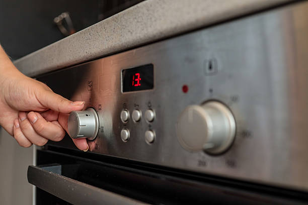istock Close-up of a woman's hand adjusting a silver control knob on a modern built-in kitchen oven with a digital display showing 2225316381