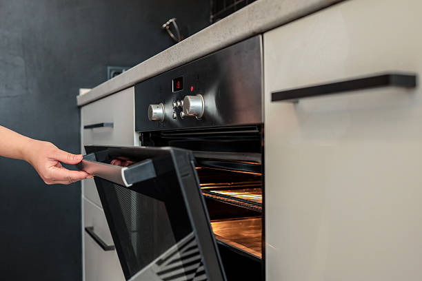 istock Woman opening a modern oven in a sleek kitchen. The oven interior is illuminated and ready for baking. Hand carefully pulls the handle, revealing the warm, glowing racks inside 2225316384