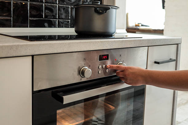 istock Person setting time or temperature on modern built-in oven using control buttons. Oven is active and glowing, with a black pot resting on the stove above 2225316390