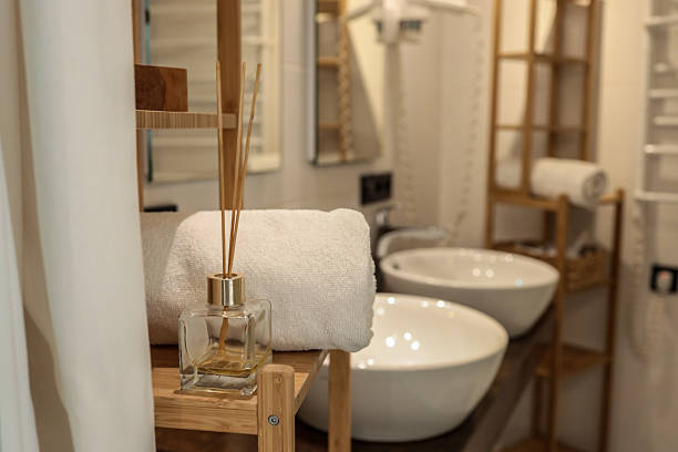 istock Minimalist bathroom interior with white towel, aroma diffuser, and modern ceramic sinks. Wooden shelving and soft lighting create a spa-like atmosphere 2225316421