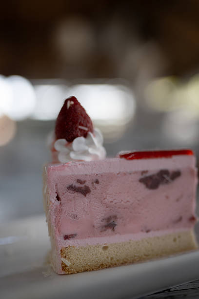A delectable slice of strawberry jelly cheesecake sitting elegantly on a rustic metal rack. The dessert features vibrant red jelly topping and creamy white cheesecake filling.