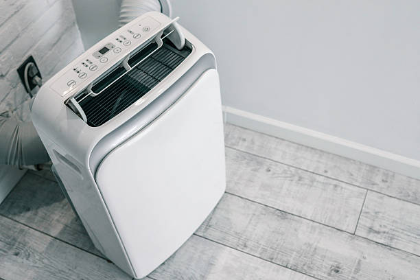 istock Close-up of a portable air conditioner with digital display and control panel, placed on a wooden floor near a wall socket 2225317867