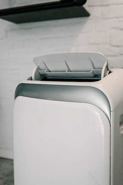 istock Close-up of a portable air conditioner with digital display and control panel, placed on a wooden floor near a wall socket 2225317871