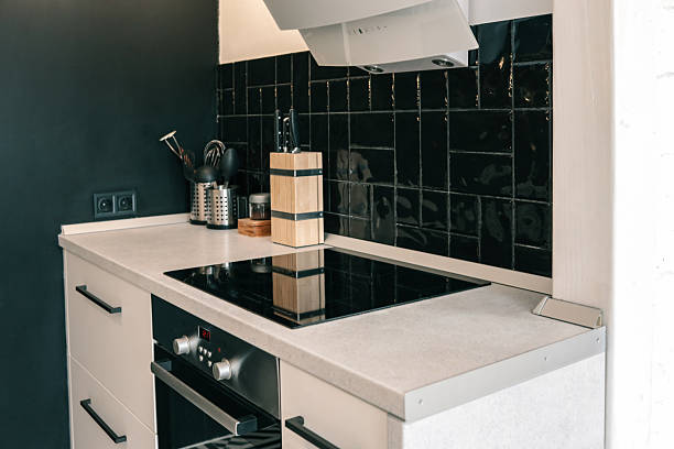 istock Modern kitchen with induction cooktop, wooden knife block, black tiled backsplash, and utensils on light countertop 2225318957