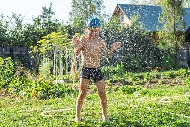 istock Joyful boy in cap washes off dirt while playing with garden hose on sunny day 2225320100