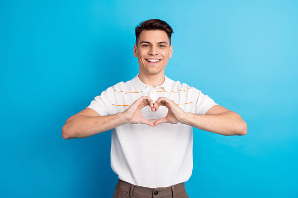 istock Young man creating a heart gesture with hands on blue backdrop symbolizing love, happiness, and positivity 2225320957
