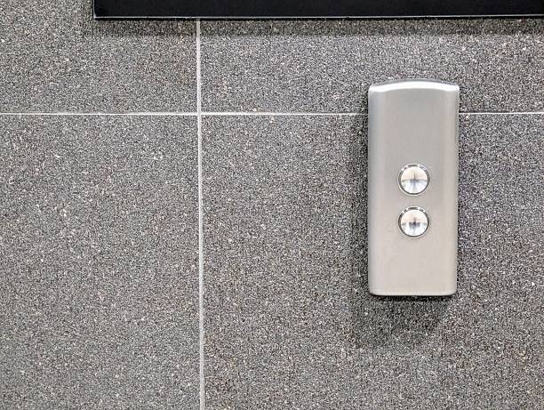 istock Close-up shot of a modern, metallic elevator call panel with two round buttons, set against a backdrop of speckled grey granite tiles 2225321295
