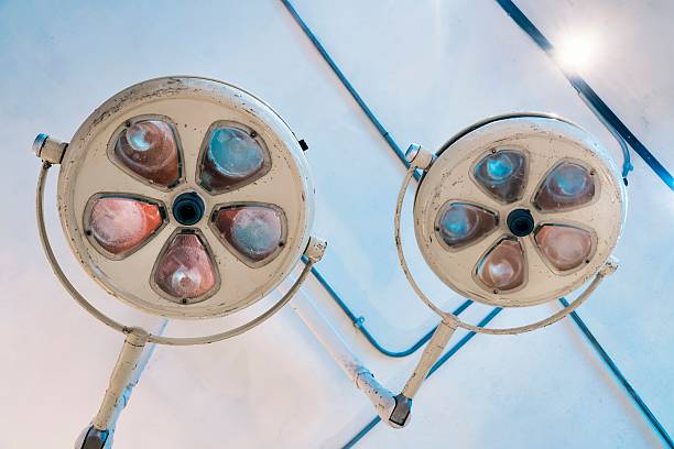 Two dusty surgical lamps hang from the ceiling of an abandoned operating room in a old hospital