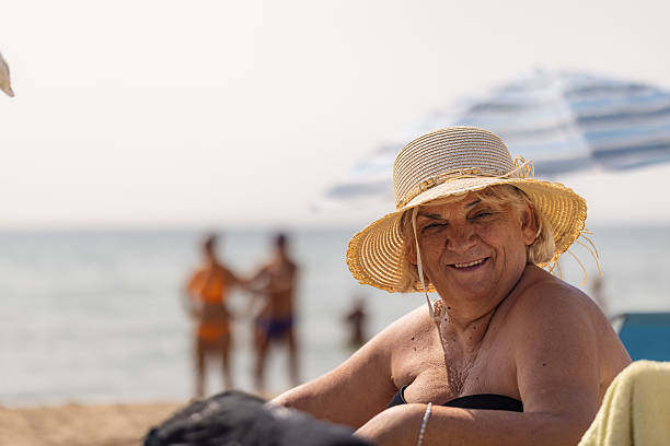 A radiant portrait of a smiling older woman wearing a straw hat, captured in a moment of pure joy on the beach.