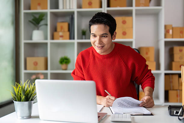 istock E-commerce Success. Smiling young man reviewing documents in home office. 2225330850