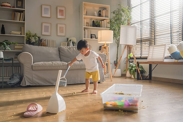 Cute little toddler boy helping his mom with housework, sweeping the dusty floor using a broom. Young child learning responsibility through cleaning tasks at home, engaging in fun and helpful household chores.