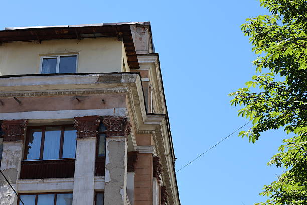 Elegant old building features intricate details and a weathered facade against a bright blue sky. The lush greenery adds vibrant color to the urban scene during daytime.