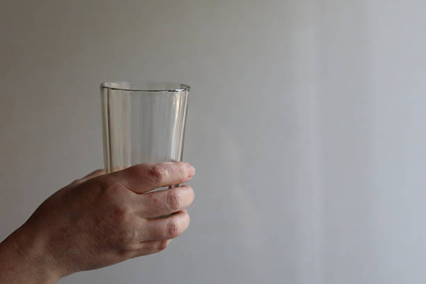 Hand holding a clear glass against a neutral background in a bright room