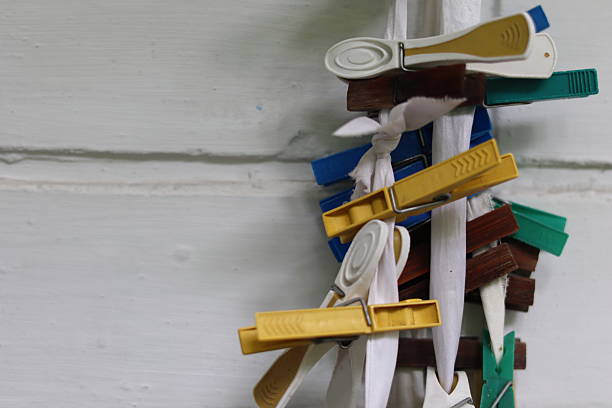 Clothespins in various colors are clipped onto a white clothesline, creating a vibrant display against a simple wall. The setting suggests a homey laundry area.