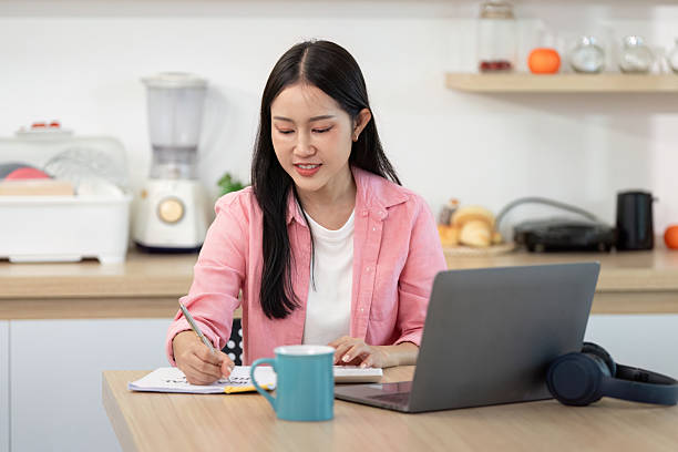 Remote Work. Young woman working from home, taking notes and focused on laptop.