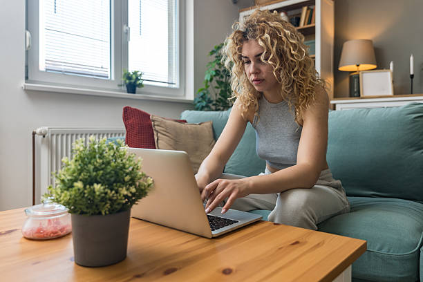 istock Concentrated millennial girl sit on couch working on laptop browsing internet at home during lazy weekend, focused young woman freelancer busy using computer surfing wireless web shopping online 2225338462