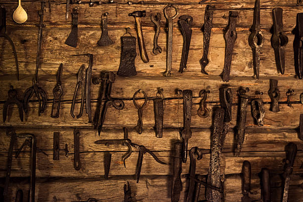Various antique tools hang on a weathered wooden wall in a workshop, showcasing a rich history of craftsmanship and manual work in a cozy environment.