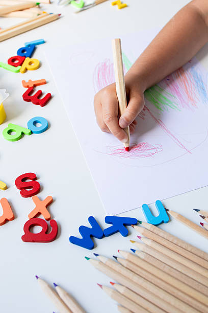 istock Child drawing with colored pencils and alphabet letters on white surface 2225342264