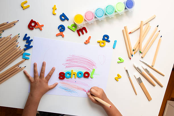 istock Child drawing with colorful letters, crayons, and paints on white table 2225343460