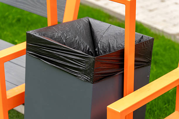 istock Trash bin with black liner and bright orange frame sits near a park bench, emphasizing urban public space cleanliness in sunny weather 2225346386