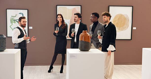 istock Man, explain and people with champagne at gallery for event, audience chat and talking for auction. Curator, customer and alcohol for discussion, artwork collection and art presentation of exhibition 2225352654