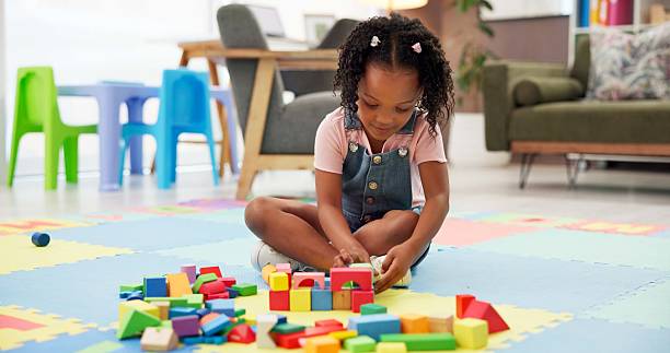 istock Kid, block and building with toys at office for fun activity, assessment or playing on floor. Black girl, child or student with shapes for playful learning, fine motor skills or elementary education 2225352949
