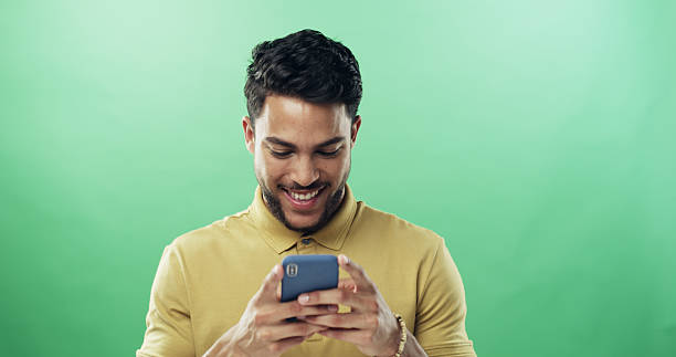 istock Man, phone and happy with texting in studio with notification, meme and laugh by green background. Person, smile and scroll with smartphone on mobile app, mockup space and funny video on social media 2225353220